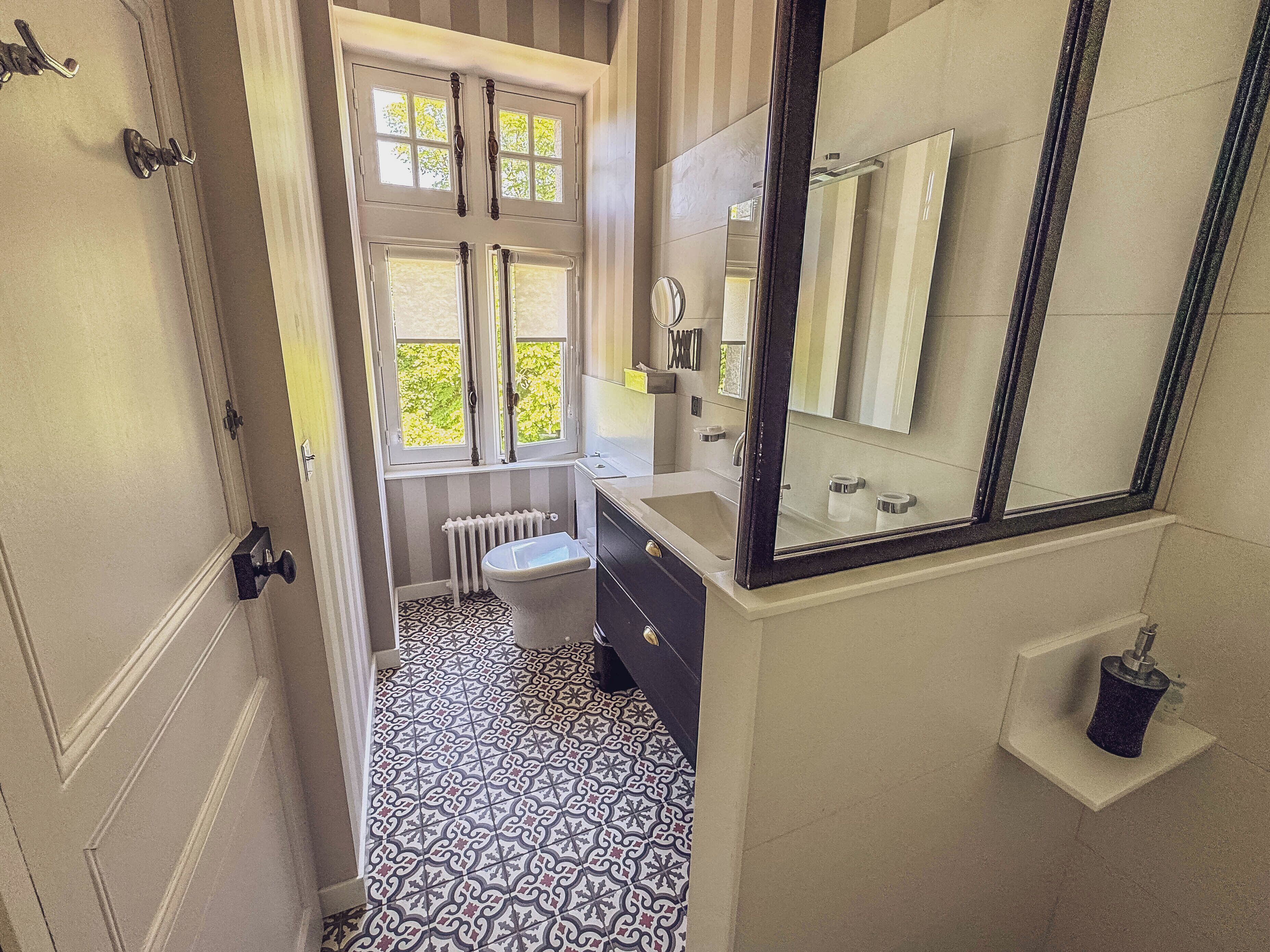 A bathroom with a white and black patterned floor, a white sink, a mirror, and a radiator.