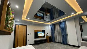 Habitación de hotel moderna con televisor de pantalla plana, cama, sofá y balcón con cortinas.