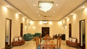 A spacious dining area with a chandelier, ceiling fan, and multiple seating arrangements including sofas and dining tables. - Aroma Green Resort (Gurugram)