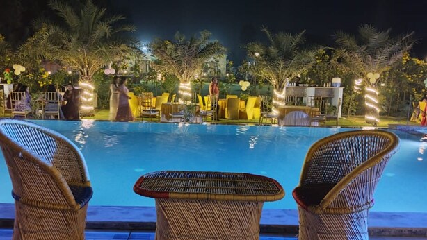 A poolside area with wicker chairs and tables, surrounded by palm trees and outdoor lighting. - Aroma Green Resort (Gurugram)