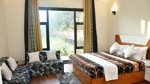 A bedroom with a large bed, a sofa, and a window with curtains. - Aroma Green Resort (Gurugram)