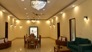 A spacious living area with a chandelier, ceiling fan, and a dining table with chairs. - Aroma Green Resort (Gurugram)