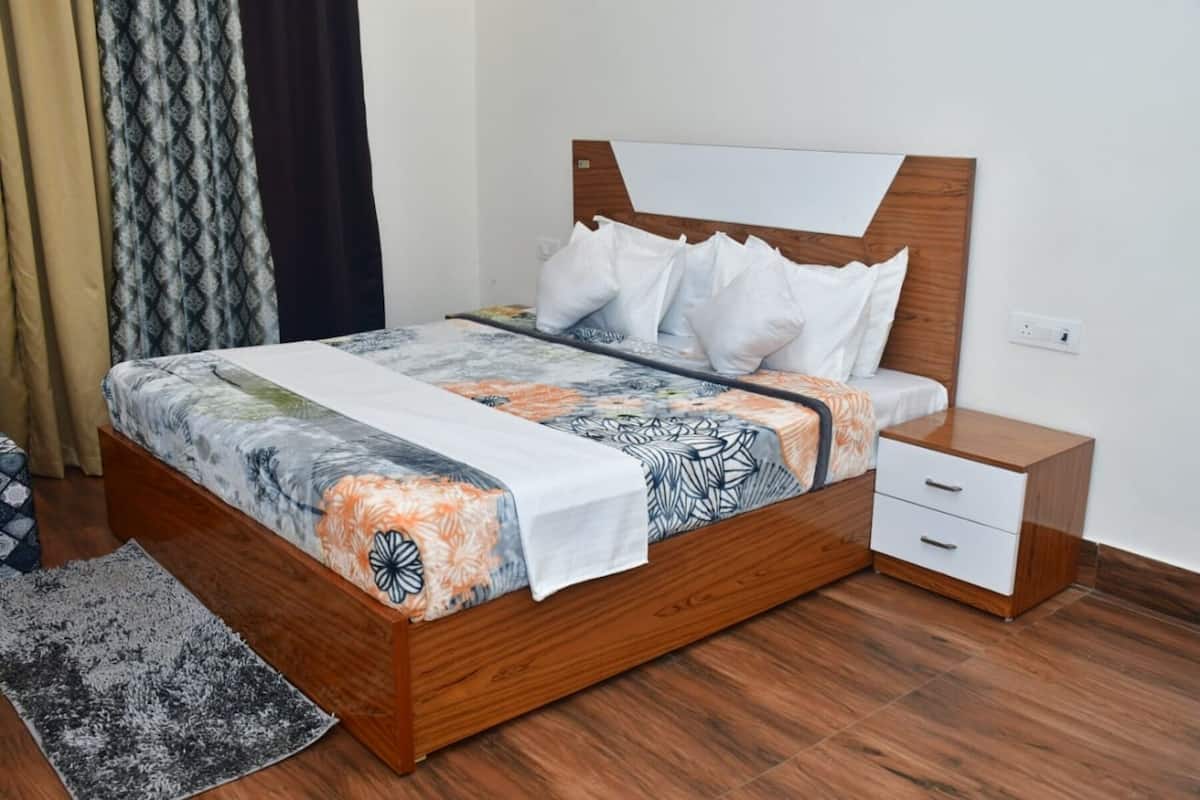 Un lit avec un cadre en bois, une literie blanche et une couvre-lit à motifs. Il y a une table de chevet avec un tiroir et un tapis sur le sol.
