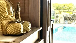 A golden Buddha statue on a wooden ledge, overlooking a swimming pool.