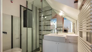 Ein modernes Badezimmer mit einer in Glas eingefassten Dusche, einem weißen Waschbecken mit Spiegel und einem weißen Heizkörper.