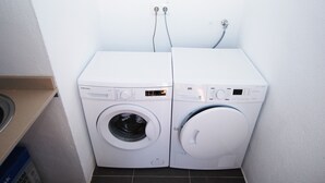 Un área de lavandería compacta con dos lavadoras de carga frontal y una secadora, equipada con paneles de control y enchufes en la pared.