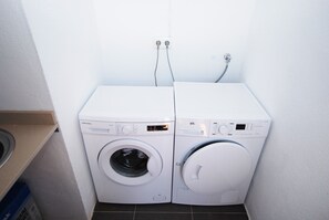 A compact laundry area with two front-loading washing machines and a dryer, equipped with control panels and power outlets on the wall.