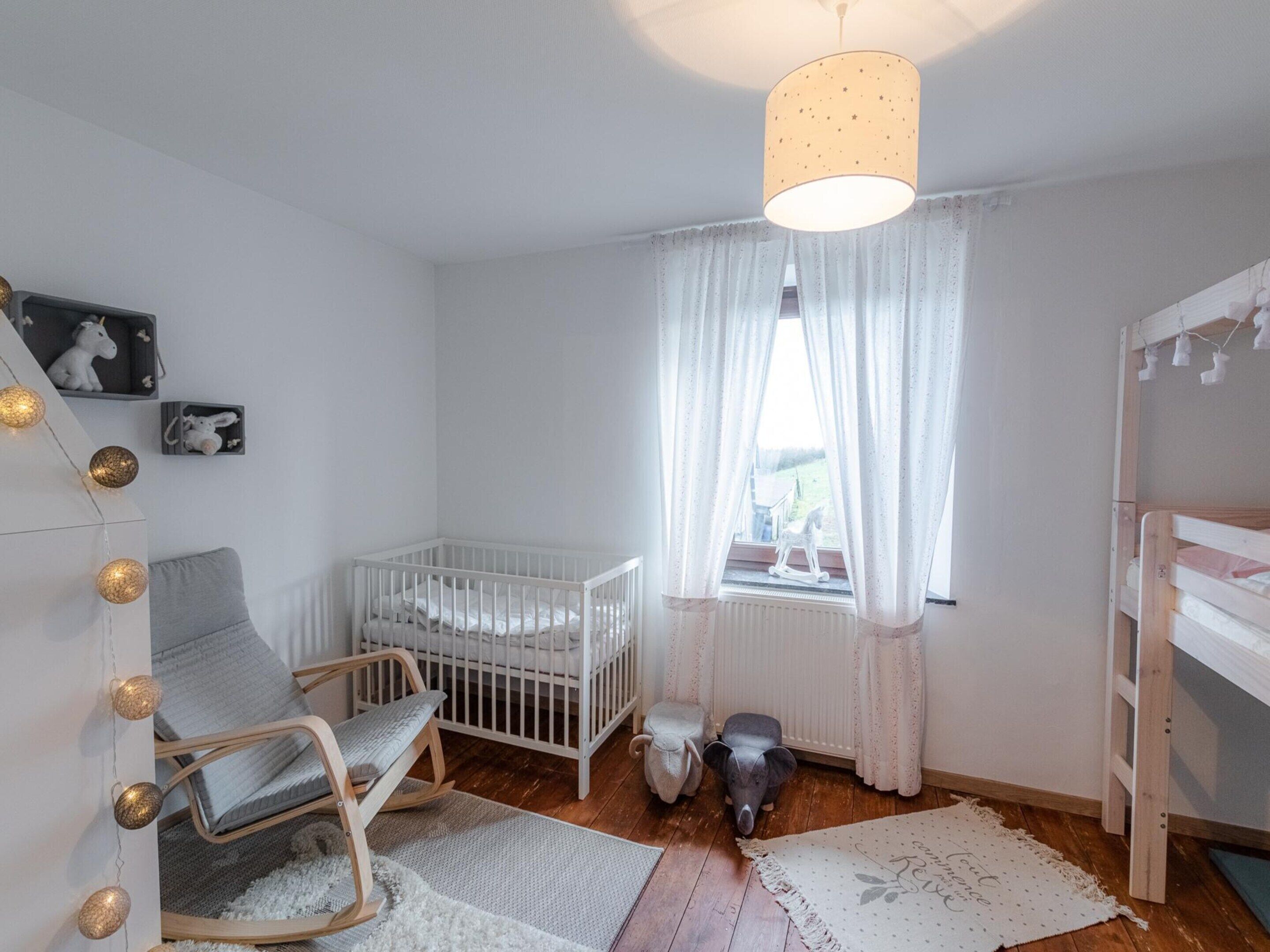 A baby room with a crib, rocking chair, and a window with curtains.