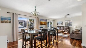 A modern living room with a dining area, wooden flooring, and large windows offering a view of the outdoors.