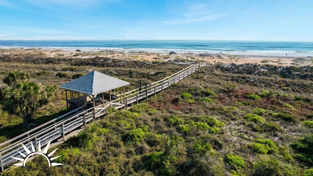 A beach view with a wooden boardwalk leading to a gazebo.