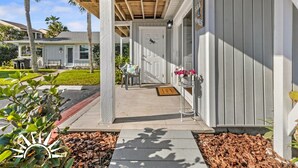 A covered porch with a bench, a door, and a small table with flowers.