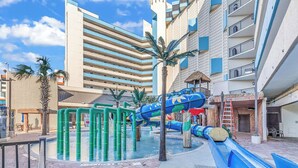 A pool area with a water slide and play structures, surrounded by buildings with balconies and palm trees. - The Sands at Ocean Reef (Myrtle Beach)