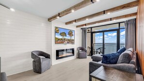 A modern living room with a fireplace, comfortable seating, and a balcony with a view. - The Sands at Ocean Reef (Myrtle Beach)