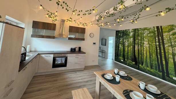 Una cocina moderna con comedor, armarios de madera y un mural con motivos forestales en la pared.