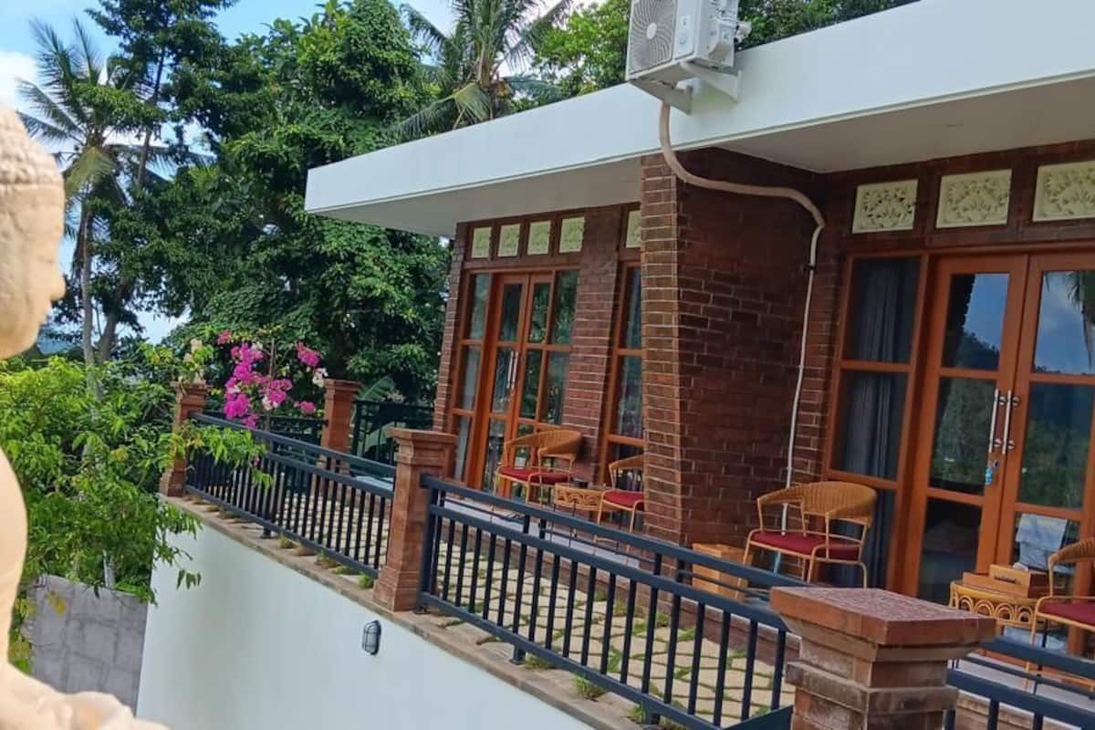Un edificio con una estatua de Buda, un balcón con sillas y vistas a zonas verdes.