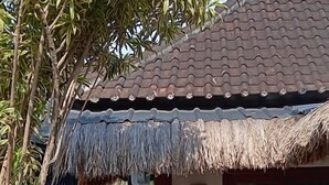 Ett traditionellt hus med ett tegeltak, ett halmtak över ingången och en staty av en sittande person.
