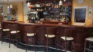 Een bar met een toonbank, verschillende barkrukken, flessenkasten en een dartbord aan de muur.