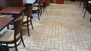 Een restaurant met tegels, houten tafels en stoelen, en een stenen muur met een televisie.