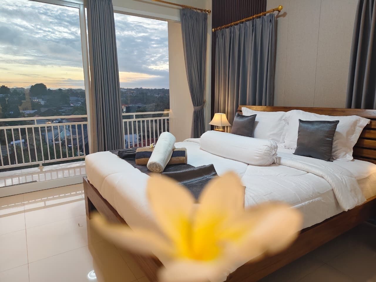 A hotel room with a large bed, a view of the city, and a balcony.