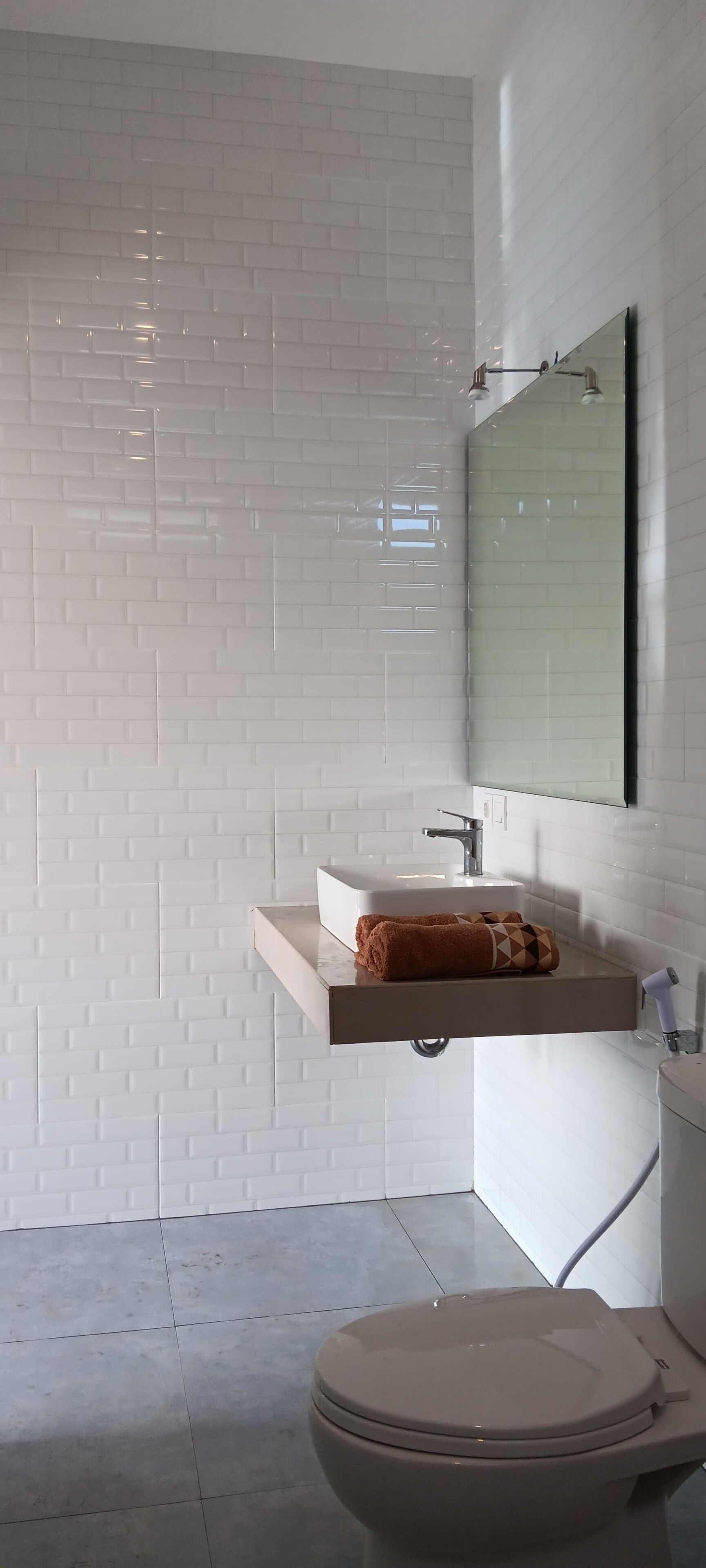 Een badkamer met witte wandtegels, een wit wastafelmeubel met een handdoek en een toilet.