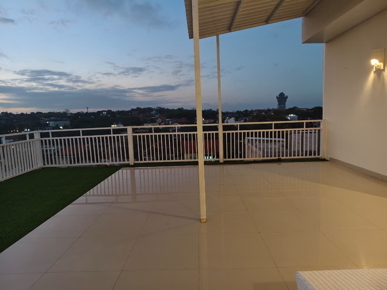 A covered outdoor area with a tiled floor, a white railing, and a view of a distant monument.