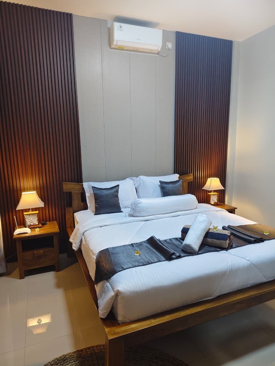 Habitación de hotel con una cama, dos lámparas de noche, aire acondicionado instalado en la pared y un cabecero de madera.
