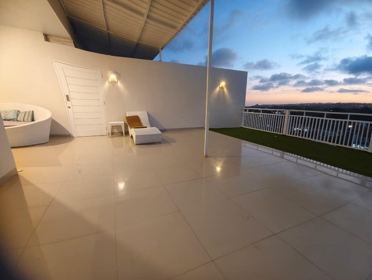 A spacious balcony with a white door, a seating area with cushions, and a railing.