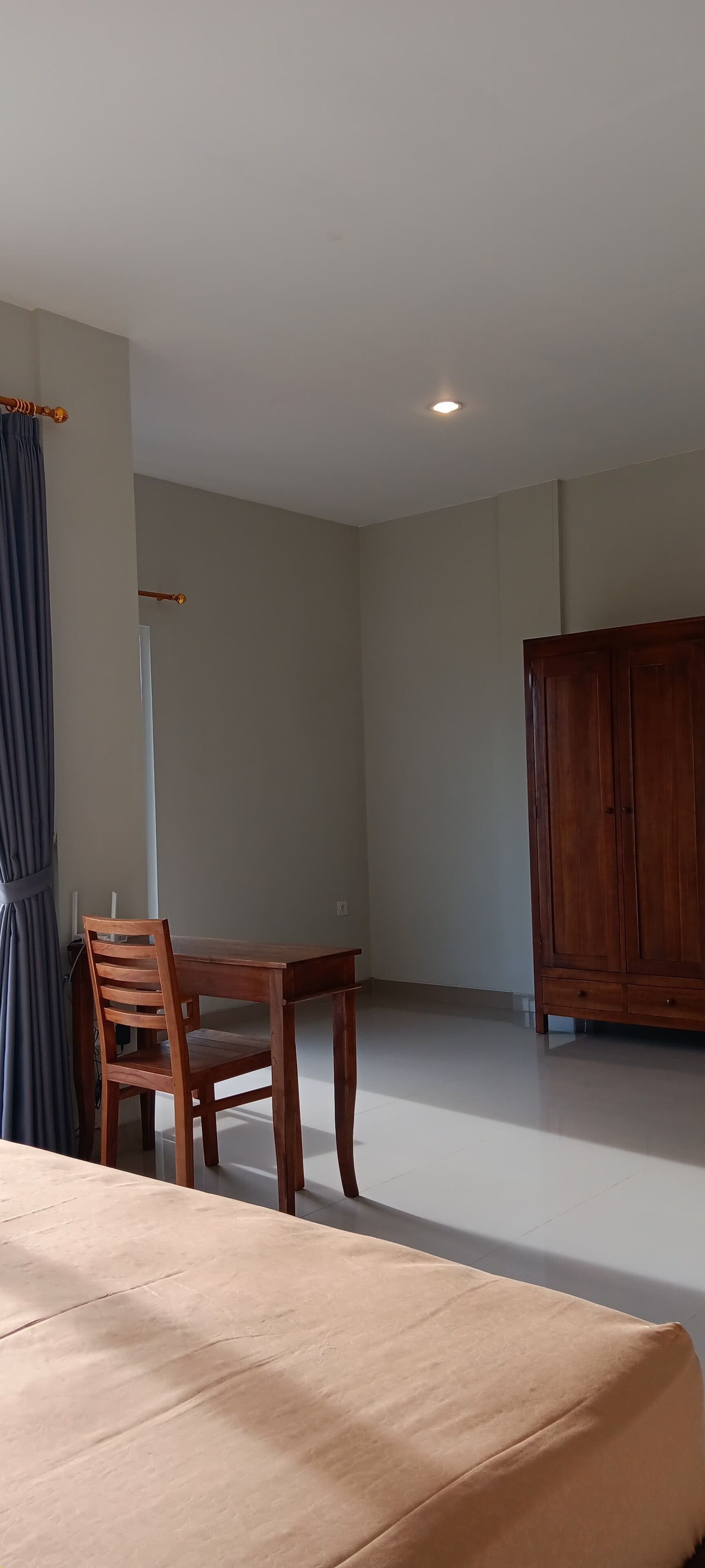 Een kamer met een bed, een houten tafel met twee stoelen, een kledingkast en een gordijn.