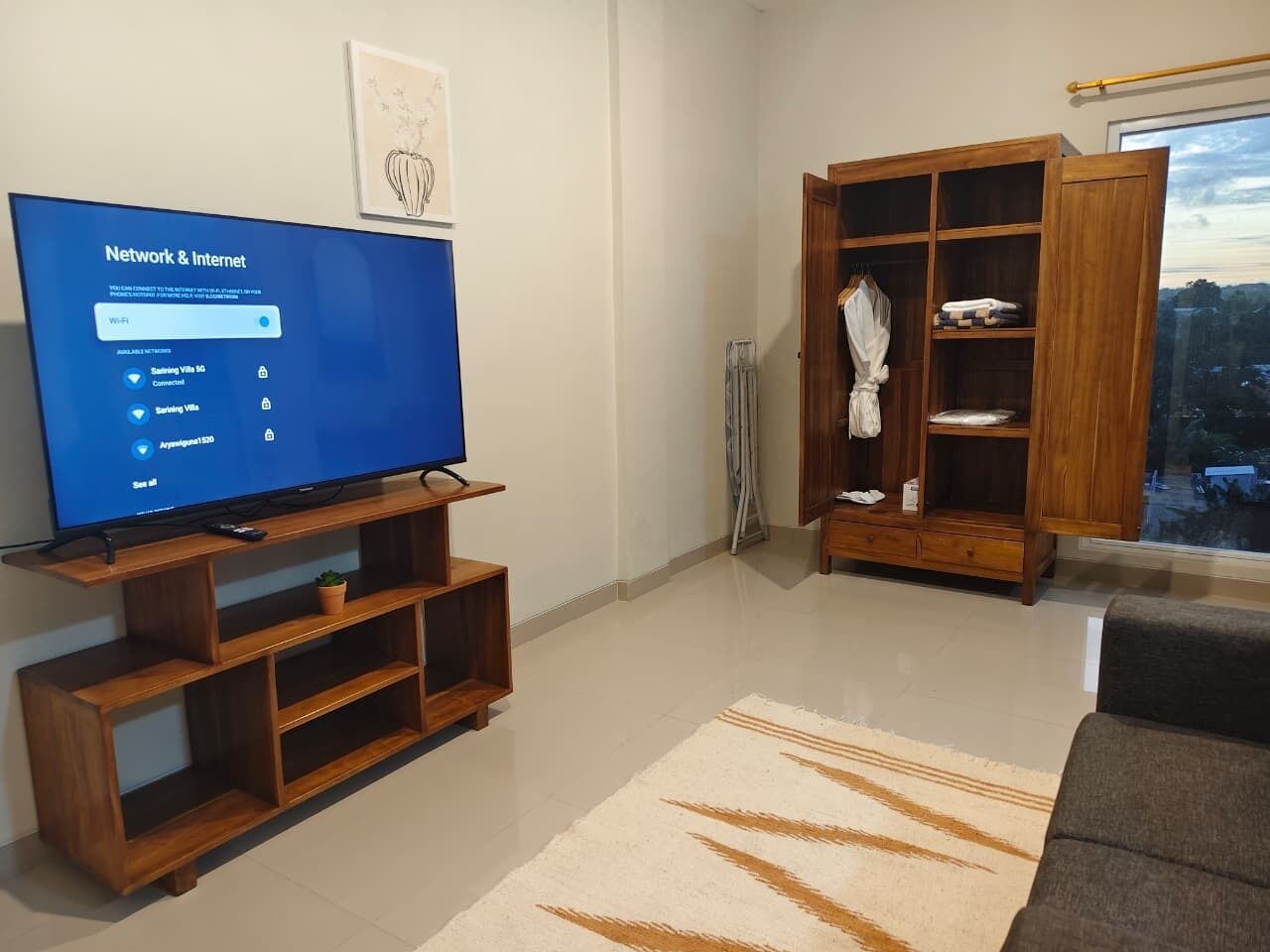 Un salon avec un téléviseur posé sur un meuble en bois, une armoire et une vue par la fenêtre.