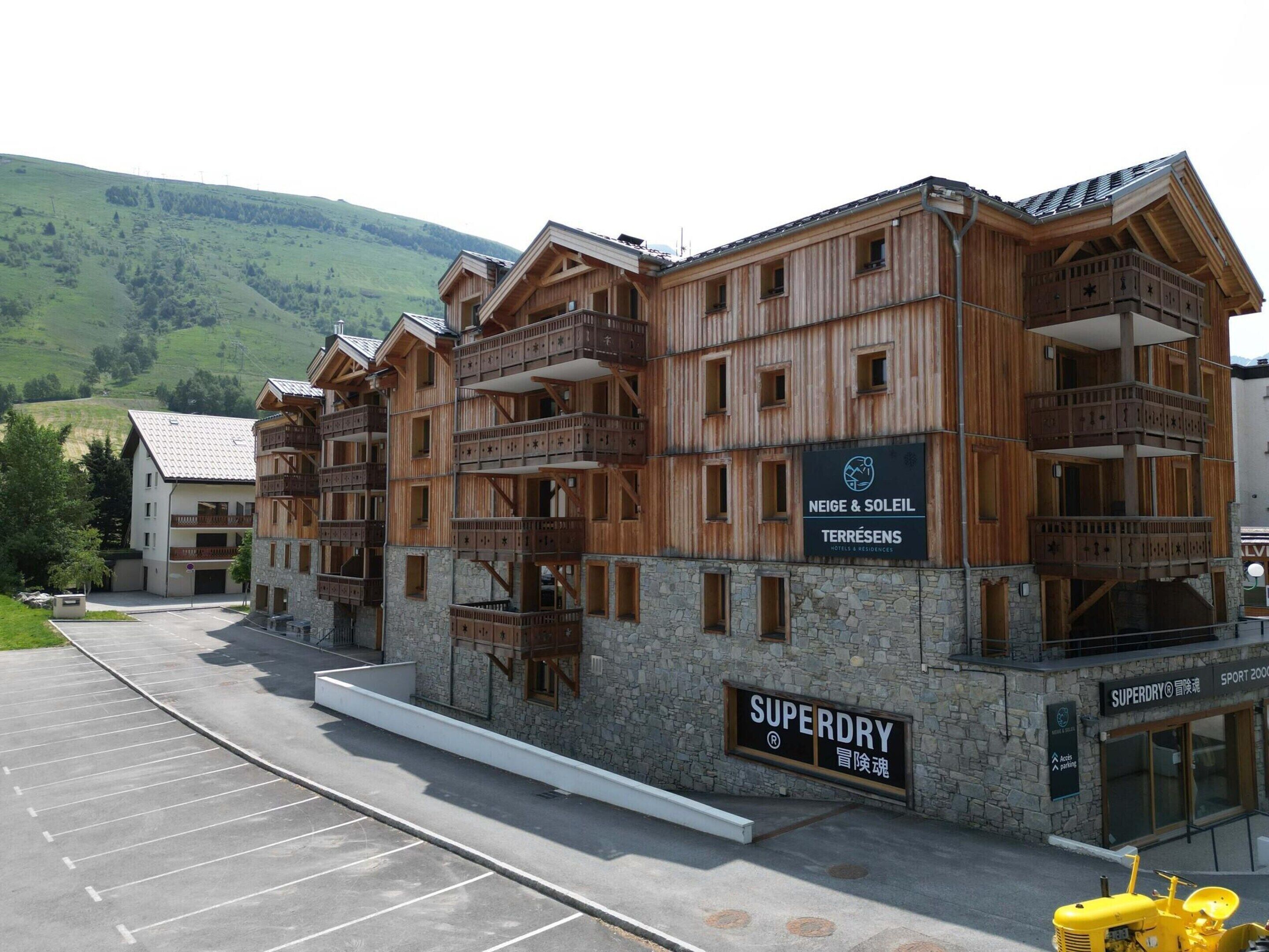 Un hôtel à plusieurs étages, doté de balcons en bois et d’une enseigne indiquant « Neige & Soleil Terrésens Hotels & Residences ».