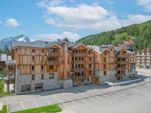 A multi-story wooden building with balconies, stone foundations, and a parking lot in front. - Apartment in Les Deux Alpes Near Glacier (Les Deux Alpes)
