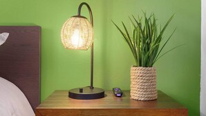 Une table de chevet avec une lampe, une télécommande et une plante en pot, le tout placé devant un mur vert.