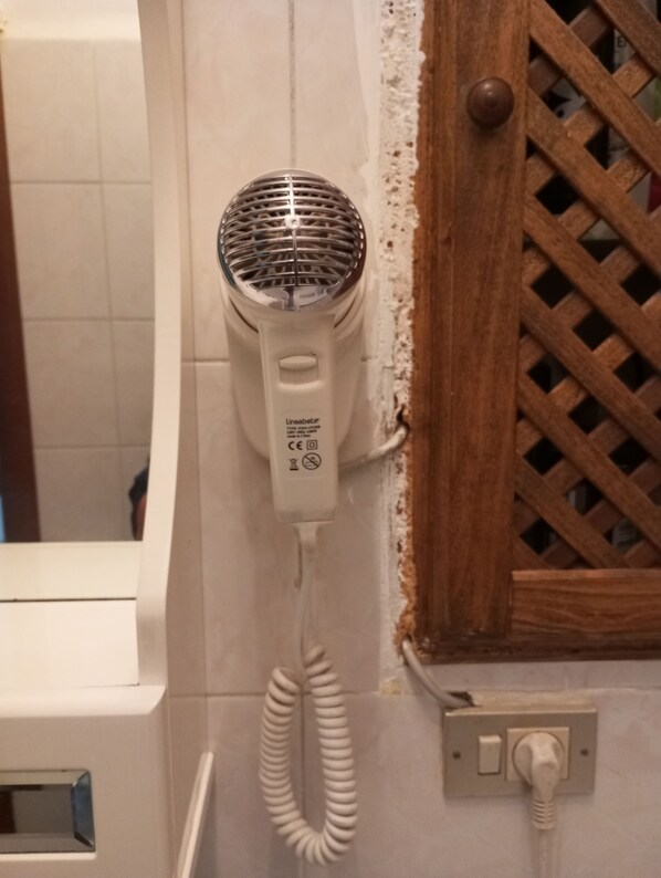 Un sèche-cheveux fixé au mur, avec un motif de treillis en bois, un mur recouvert de carreaux blancs et une porte dotée d’un cadre en bois.