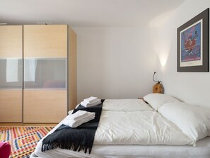 Een moderne slaapkamer met een bed, een kledingkast, een kleurrijk vloerkleed en een kunstwerk in een lijst aan de muur.