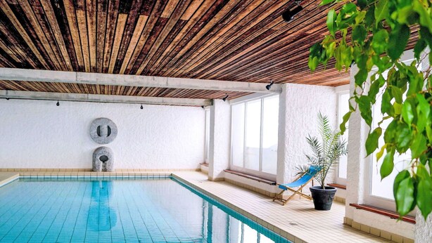An indoor swimming pool with a wooden ceiling, a blue chair, and a potted plant.