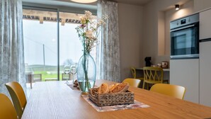 Comedor con mesa de madera, sillas amarillas, un jarrón con flores y una cesta de pan.
