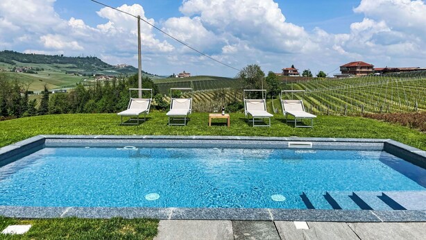 Una piscina con sillones de descanso y un viñedo al fondo.