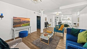 A modern living room with a television, blue and green sofas, a coffee table, and a painting of a cityscape. - Modern unit near Churchill Downs and Expo Center! (Louisville)