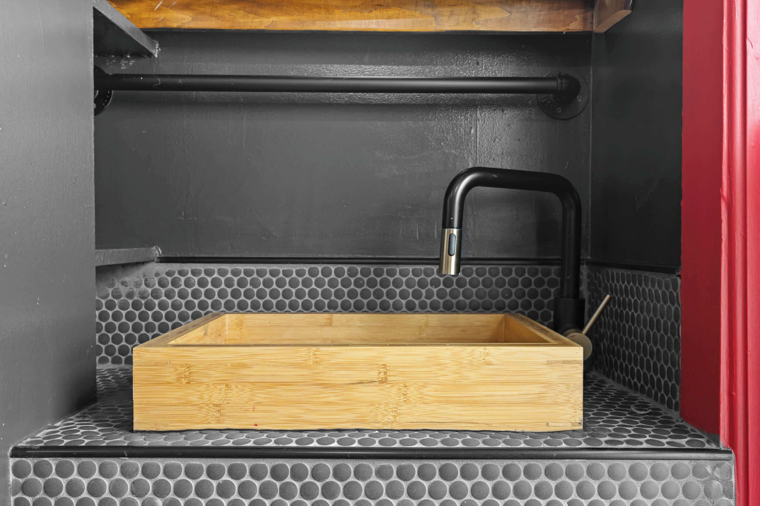 A wooden box on a textured surface with a black faucet and a metal pipe above it.