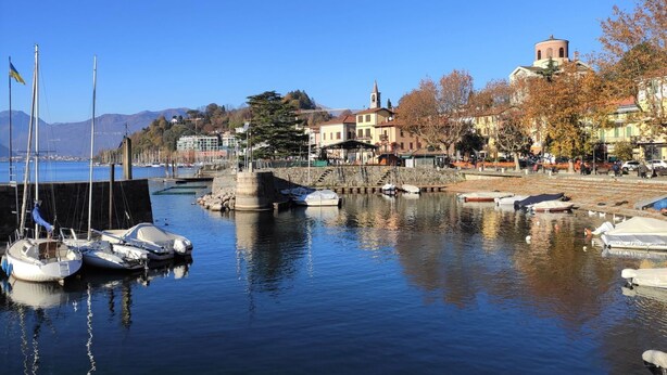 Un puerto deportivo con barcos amarrados, un muelle de piedra y edificios con una aguja de iglesia al fondo.