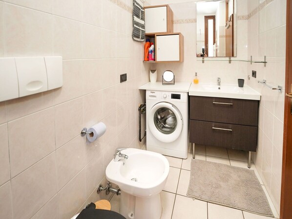 A compact bathroom with a washing machine, a sink, a toilet, and a mirror.