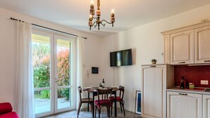 A modern kitchen with a dining area, a TV mounted on the wall, and a sliding glass door leading to a garden. - Cosy apartment for 4 people with WIFI, TV, terrace and pets allowed (Gravedona)