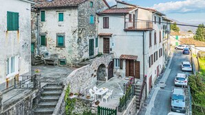 Una calle estrecha con edificios de piedra, un pequeño espacio con mesas al aire libre y coches estacionados.