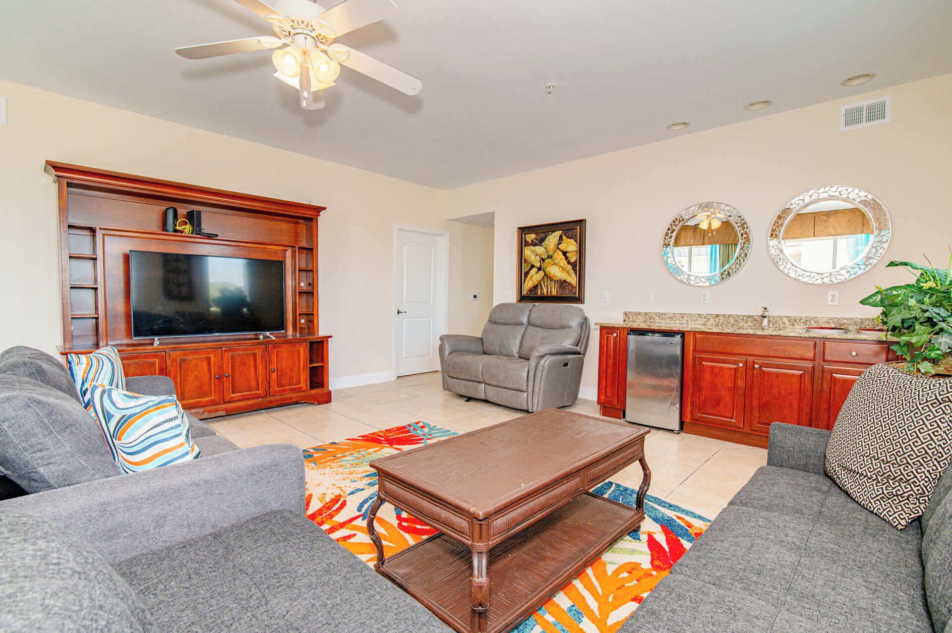 A living room with a TV, sofa, armchair, coffee table, and kitchen area.