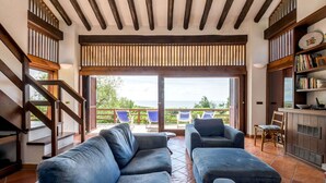 Un amplio salón con un gran sofá, una mesa de comedor y vistas al mar a través de un ventanal corredero.