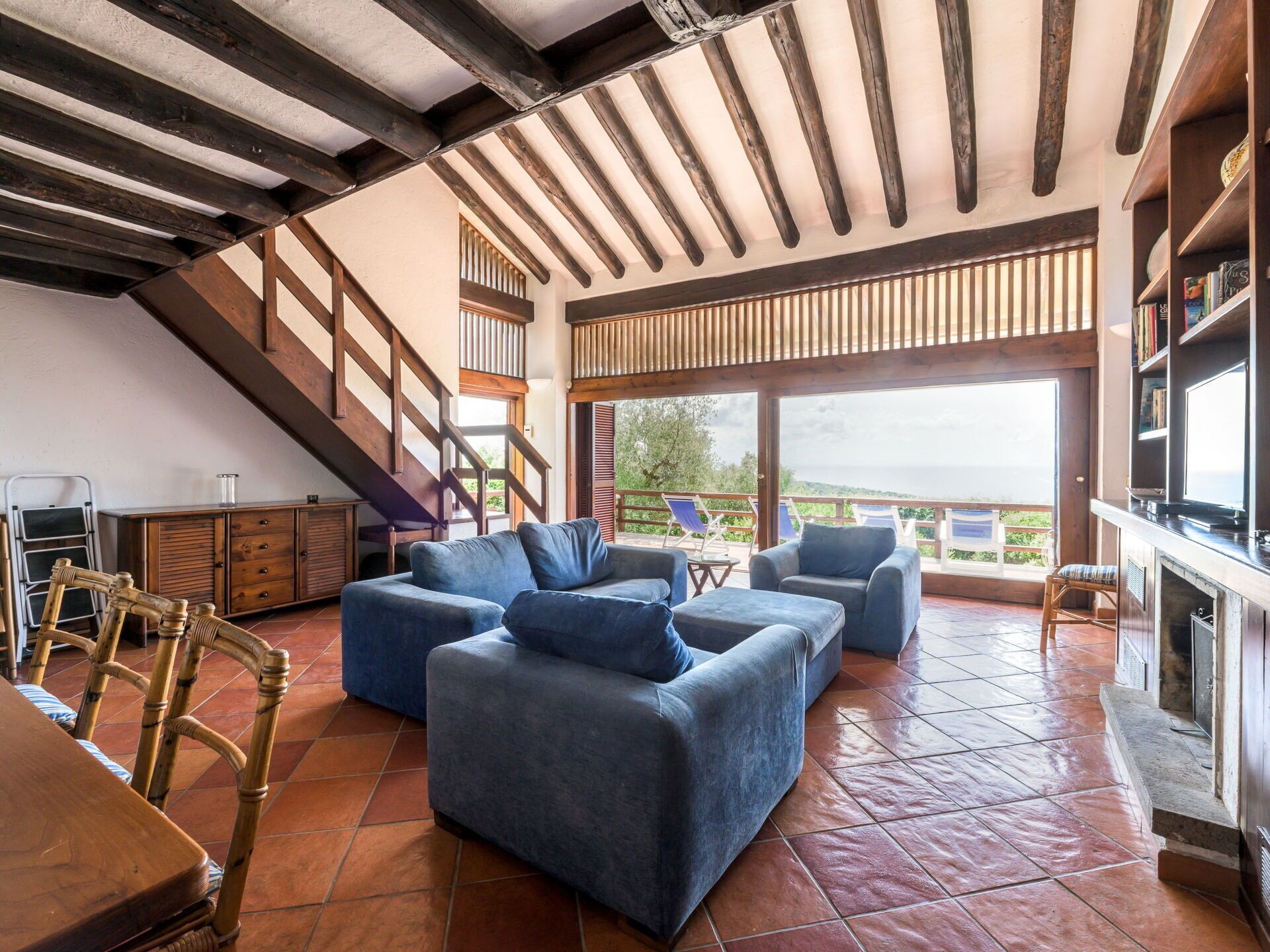A spacious living area with a high ceiling, wooden beams, a large window with a view, and a fireplace.