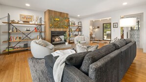 Una sala moderna con chimenea, estanterías, un sofá gris y un sillón blanco.
