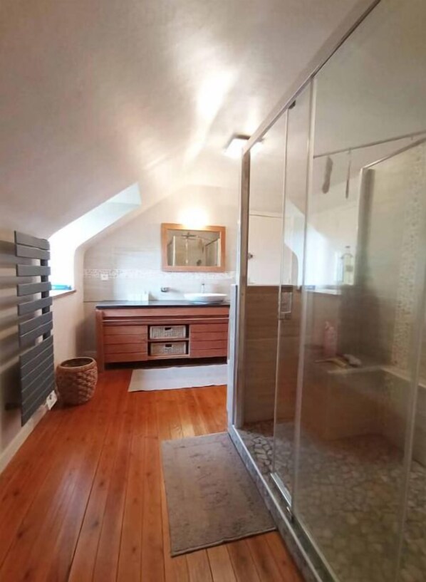 Ein schmaler, leicht abfallender Flur mit Holzdielen, einem kleinen Teppich, einem Holzschrank und einer Duschkabine aus Glas.