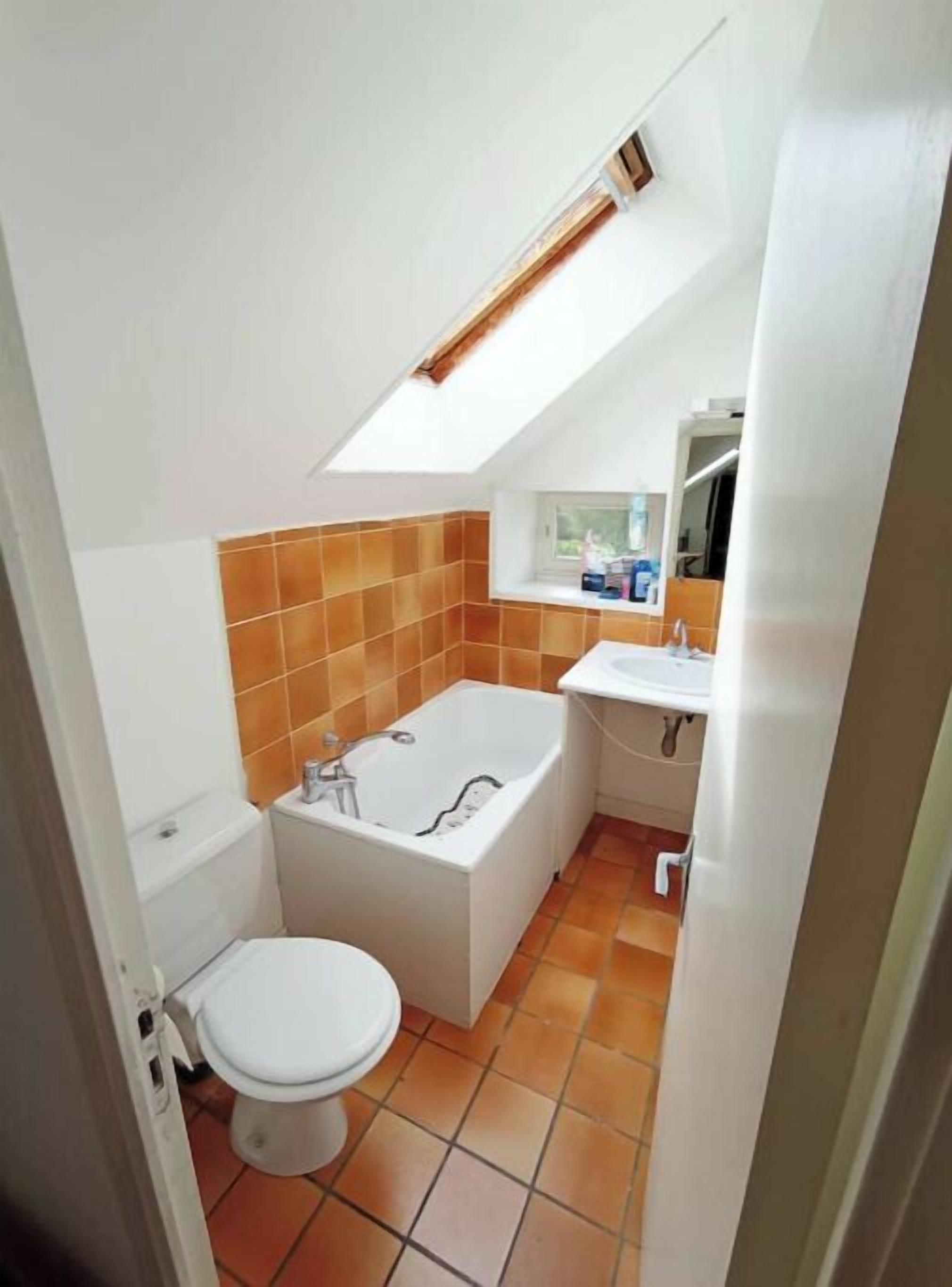 Une petite salle de bain dotée d’un puits de lumière, d’une baignoire, de toilettes et d’un lavabo.