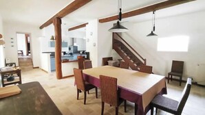 Ein geräumiger Essbereich mit einem großen Holztisch und Stühlen, einer Treppe, die zu einer oberen Ebene führt, und einer Küche im Hintergrund.